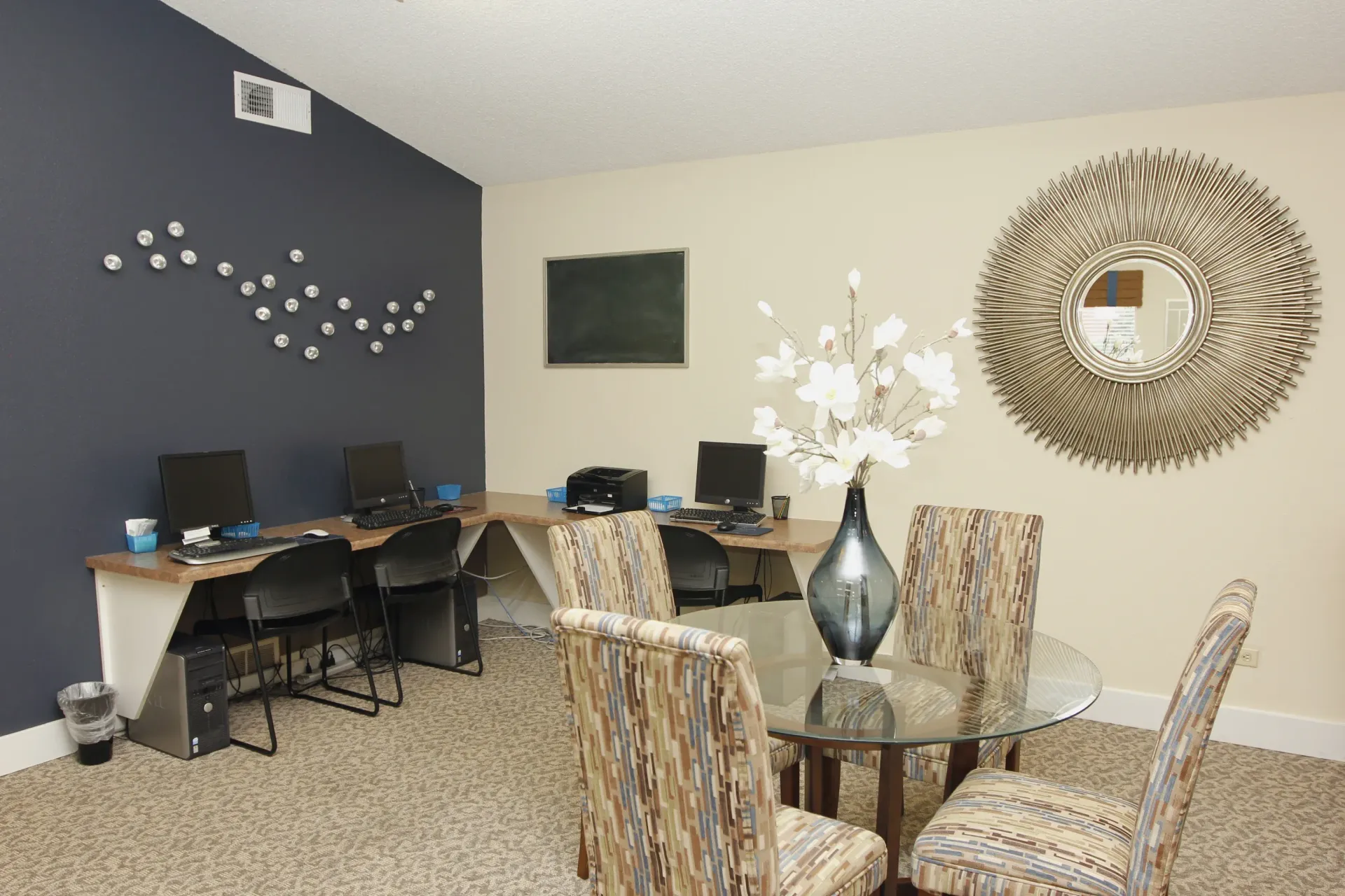 Interior community computer lounge with desks, chairs, and a round glass table.