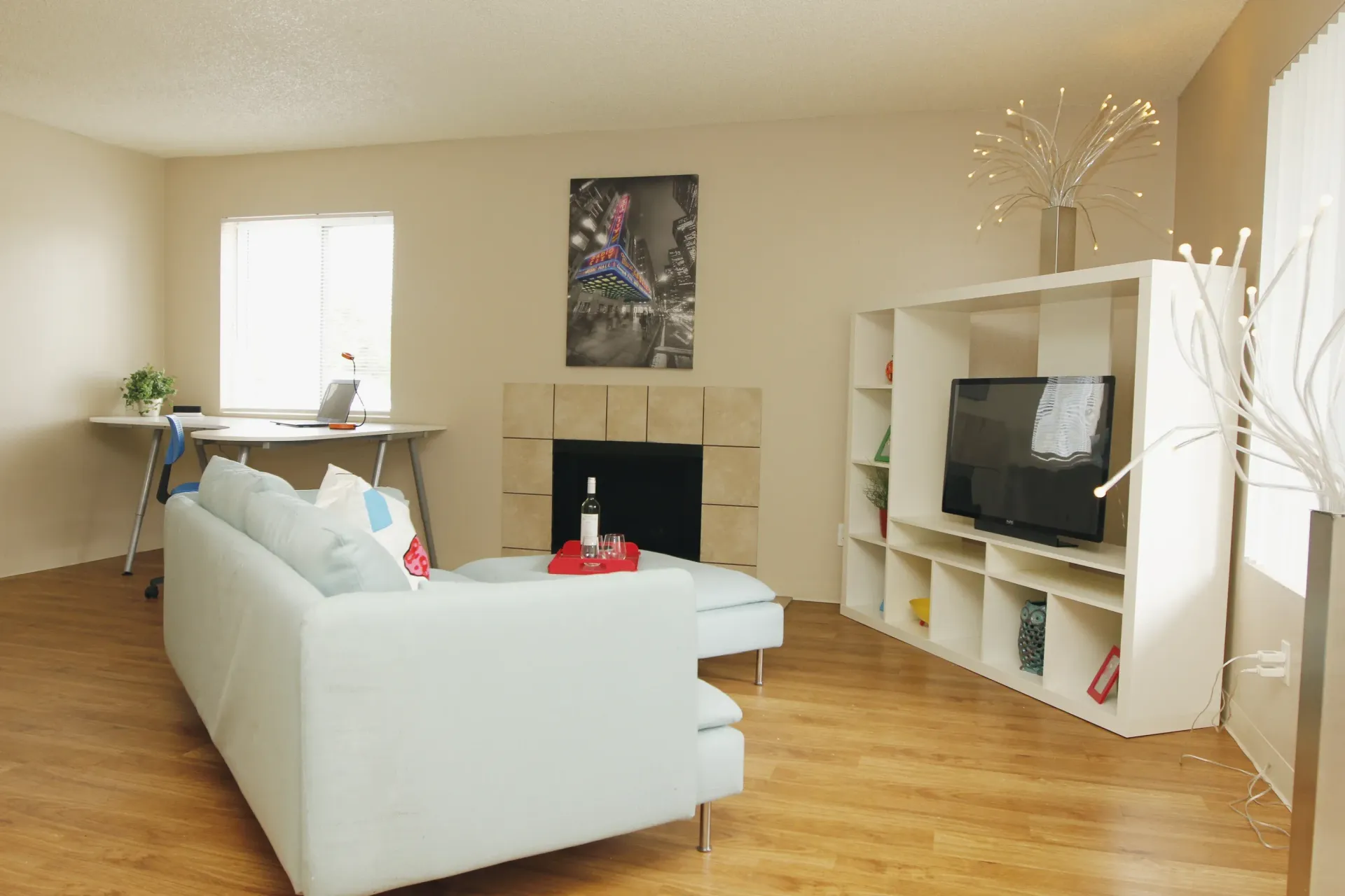 Living room with white sofa, TV, fireplace, desk, and hardwood floor.