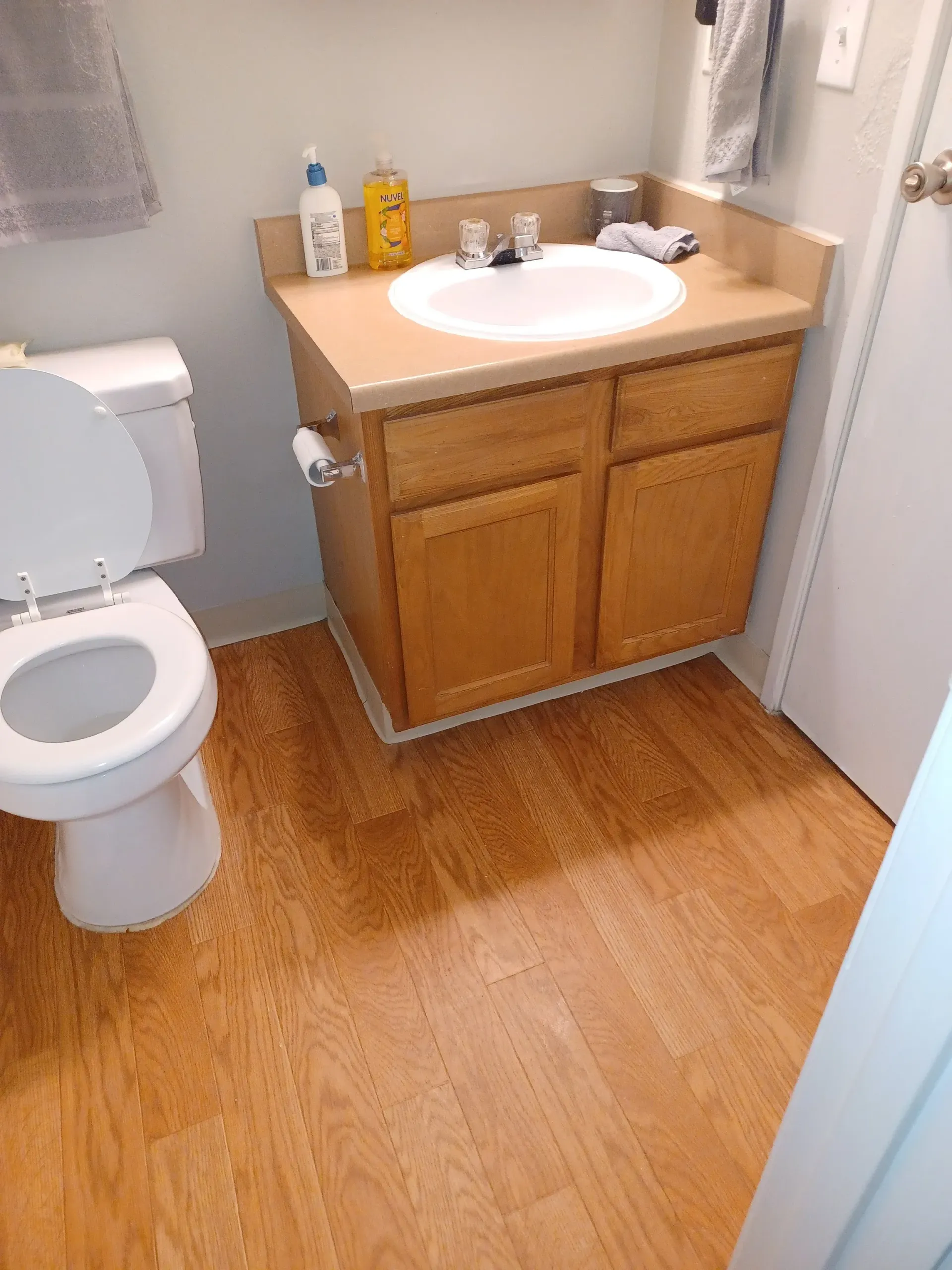 Bathroom with wooden vanity, sink, and toilet; beige countertop and towels.