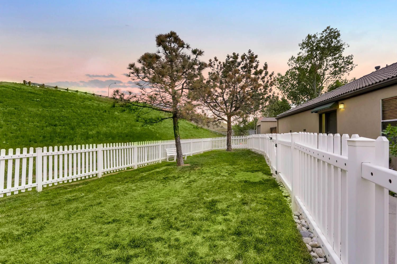 Manicured lawn with a white picket fence, two trees, and a beige apartment building on the right.