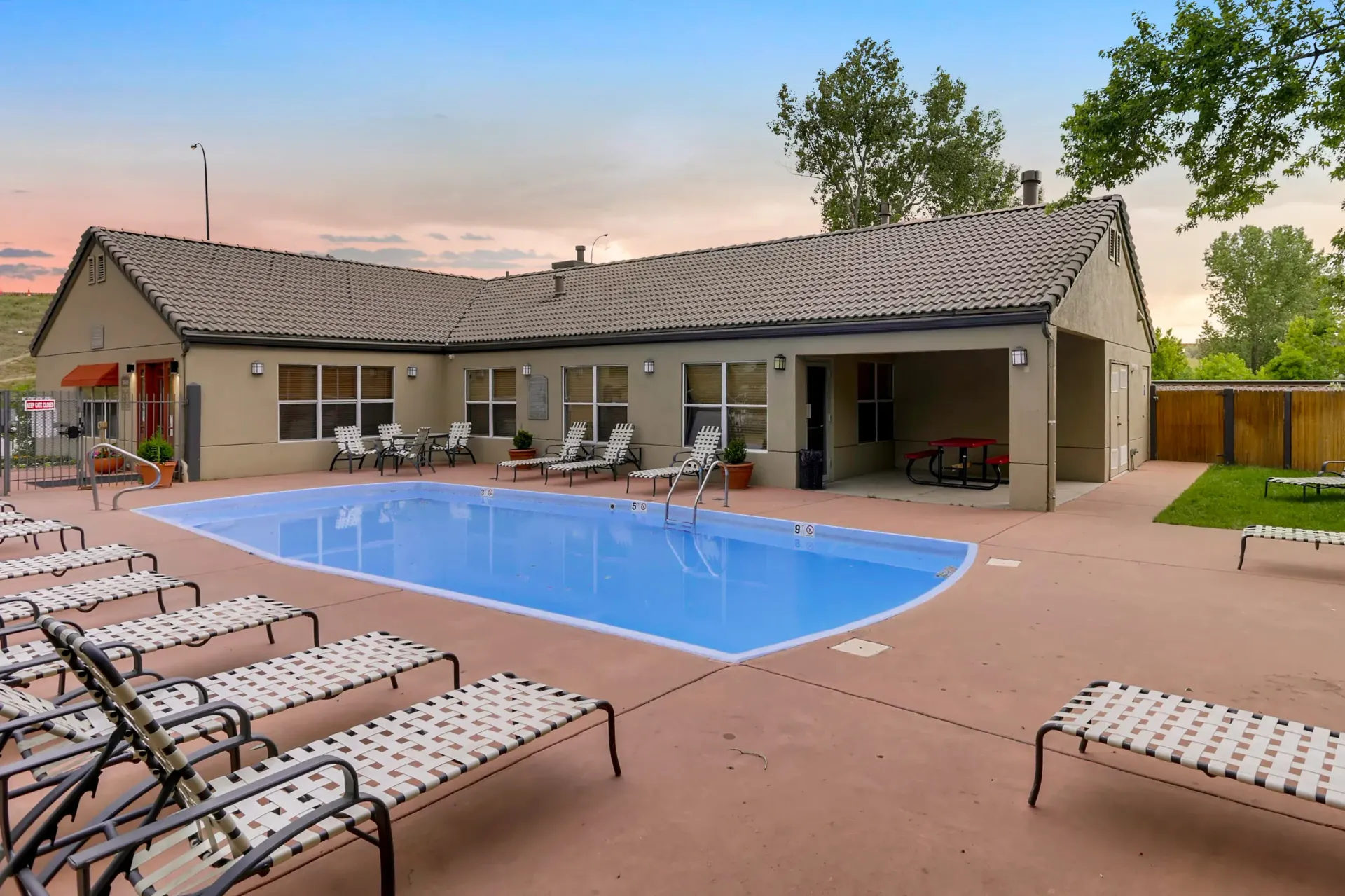 Outdoor pool area of an apartment community with lounge chairs and a shaded pavilion.