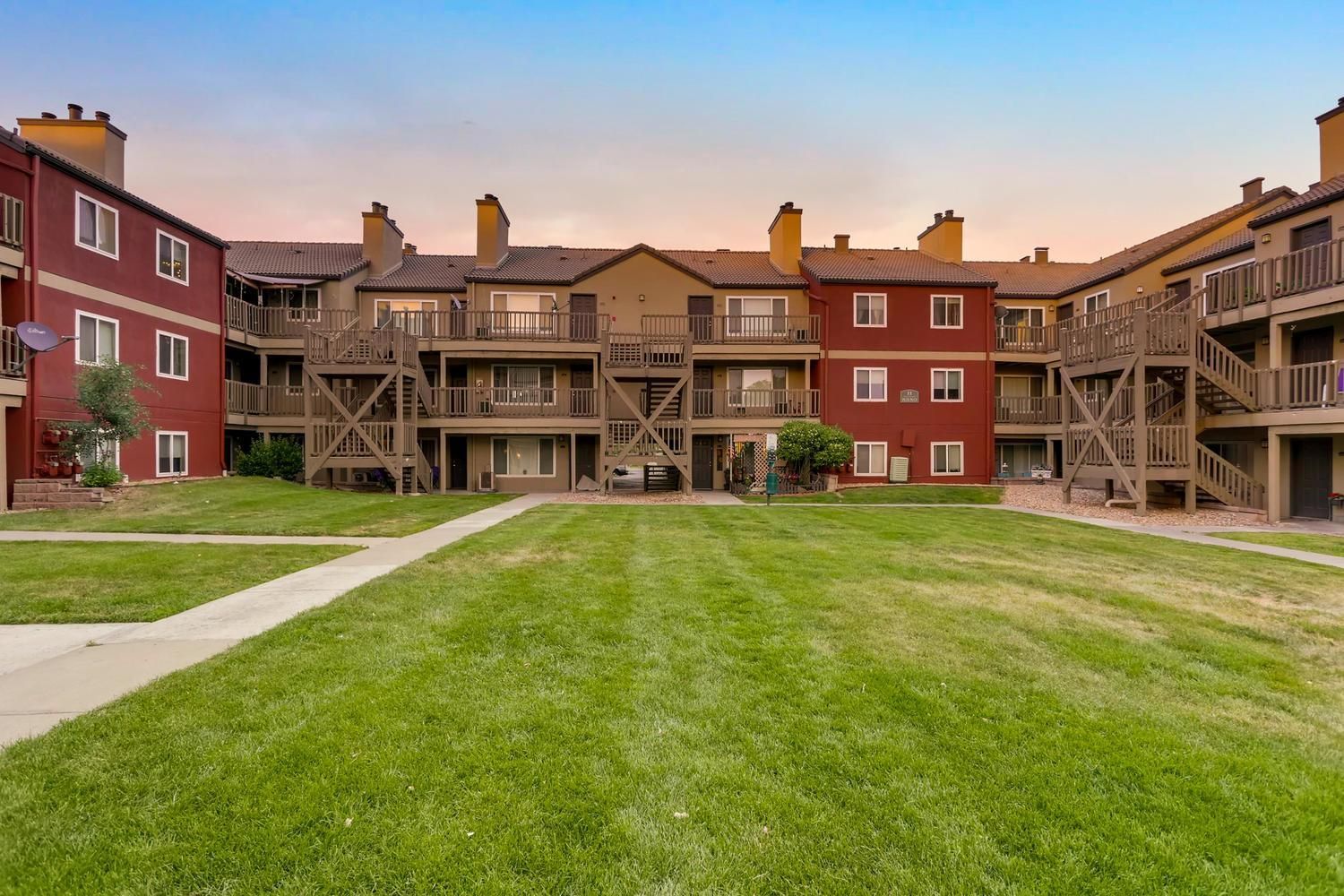 Exterior view of a multi-story apartment building with balconies and a central grassy courtyard.