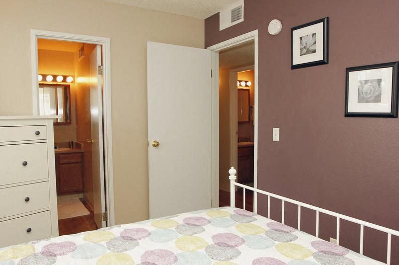 Bedroom in an apartment with a purple accent wall, bed, white dresser, and two open doors leading to a bathroom.