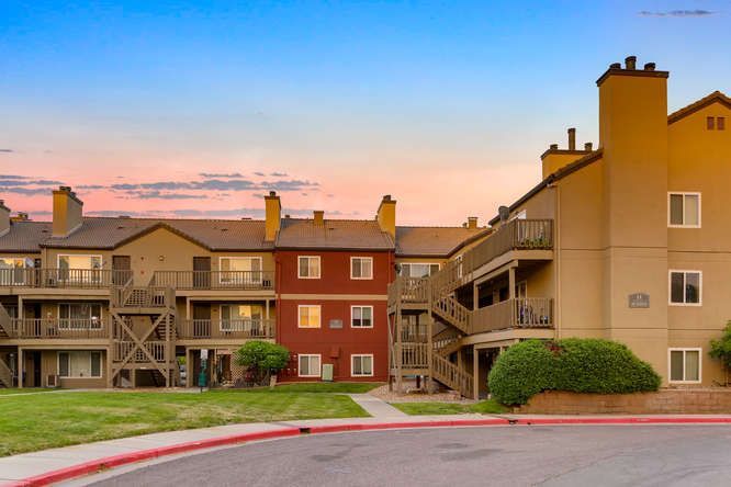 Exterior view of a multi-building apartment complex with stairwells and landscaped lawn at sunset.
