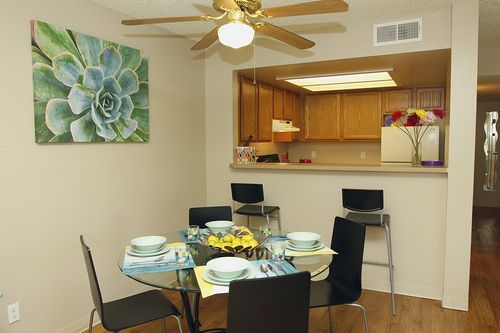 Dining area in an apartment with a round glass table, four chairs, and a kitchen pass-through.