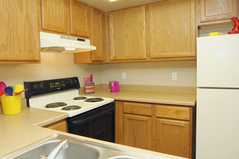 Compact apartment kitchen with wooden cabinets, an electric stove, and a white refrigerator.