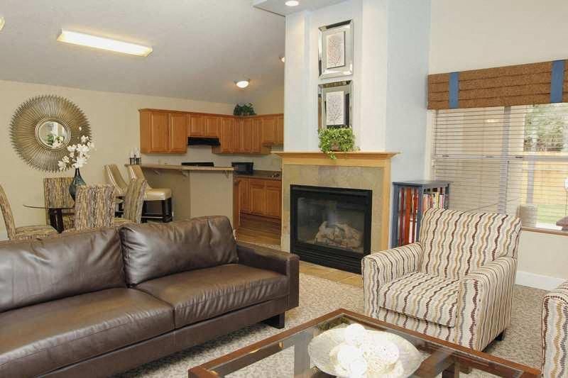 Open-concept living room with a brown leather sofa, striped armchairs, a glass coffee table, and a fireplace.
