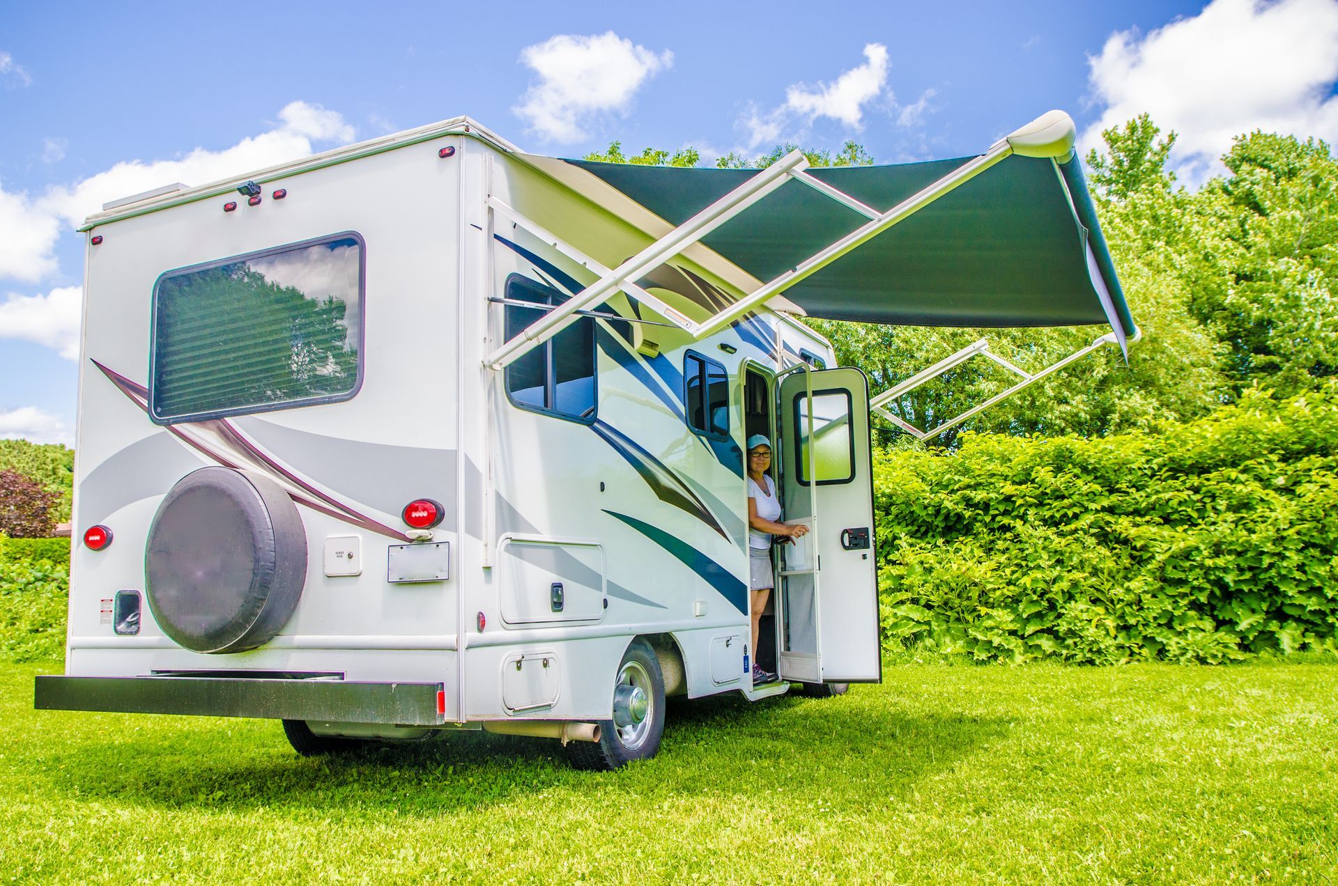 A white rv with a green awning is parked in a grassy field.