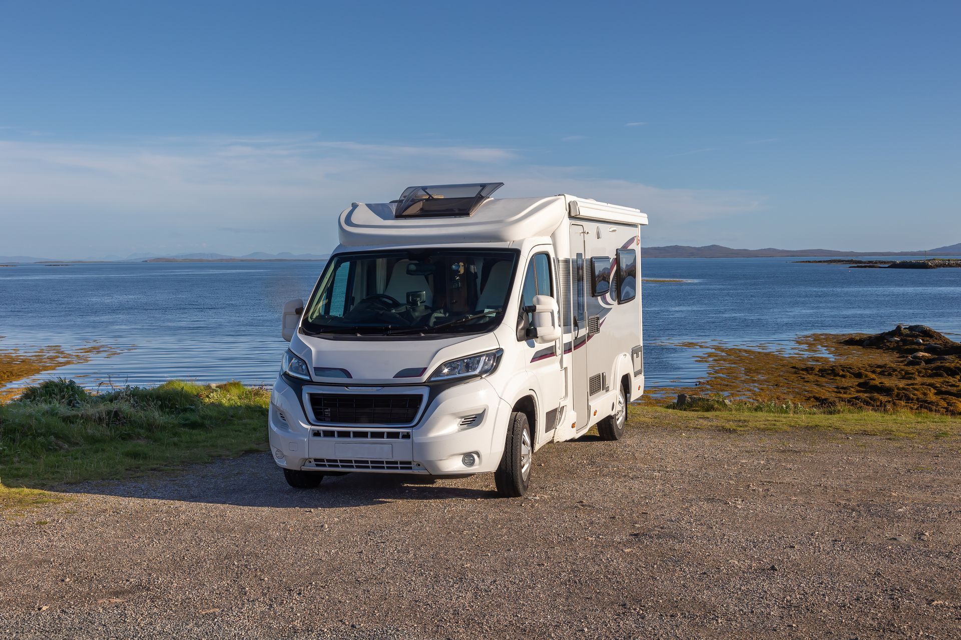 A white rv is parked on a gravel road next to the ocean.