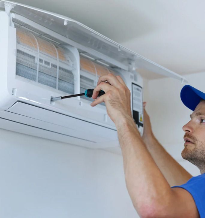 A technician uses a clamp meter to measure electrical wiring on an open HVAC unit in an indoor room.