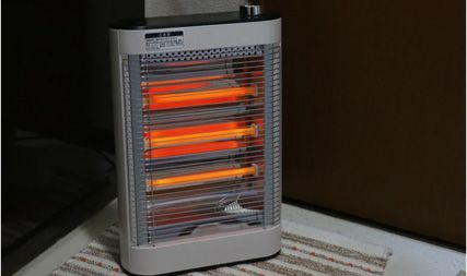 A white, rectangular electric space heater with three glowing orange heating elements sitting on a striped rug.