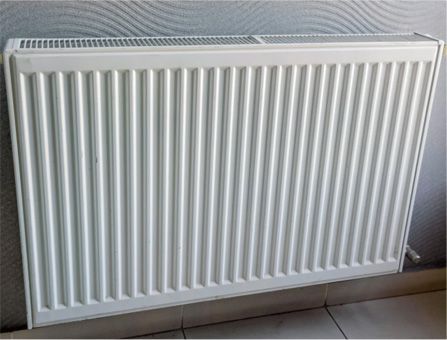 A white, rectangular ribbed panel radiator mounted on a grey wall.