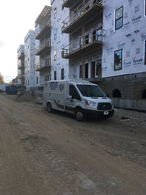 A white plumbing service van parked on a dirt construction site next to an unfinished apartment building.