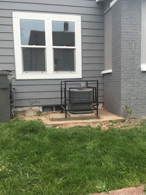 An outdoor HVAC unit enclosed in a black metal security cage against the gray siding of a house.