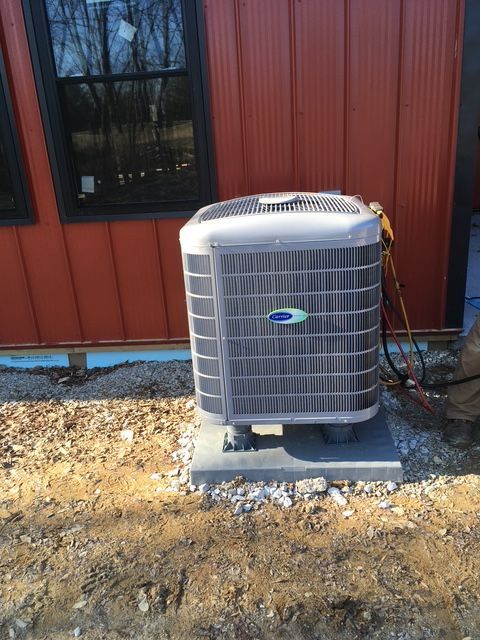 A white Carrier air conditioning unit sits on a concrete pad outside a red metal-sided building.