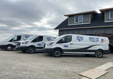 Three white Jerry Air service vans are parked in a line on a gravel lot in front of an unfinished house.