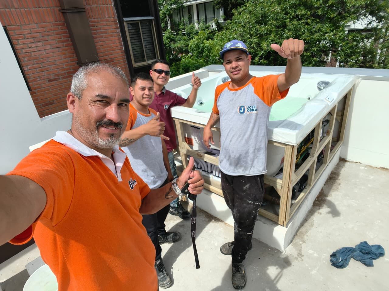 Cuatro hombres con gestos de pulgar hacia arriba junto a un jacuzzi blanco recién instalado en una azotea.