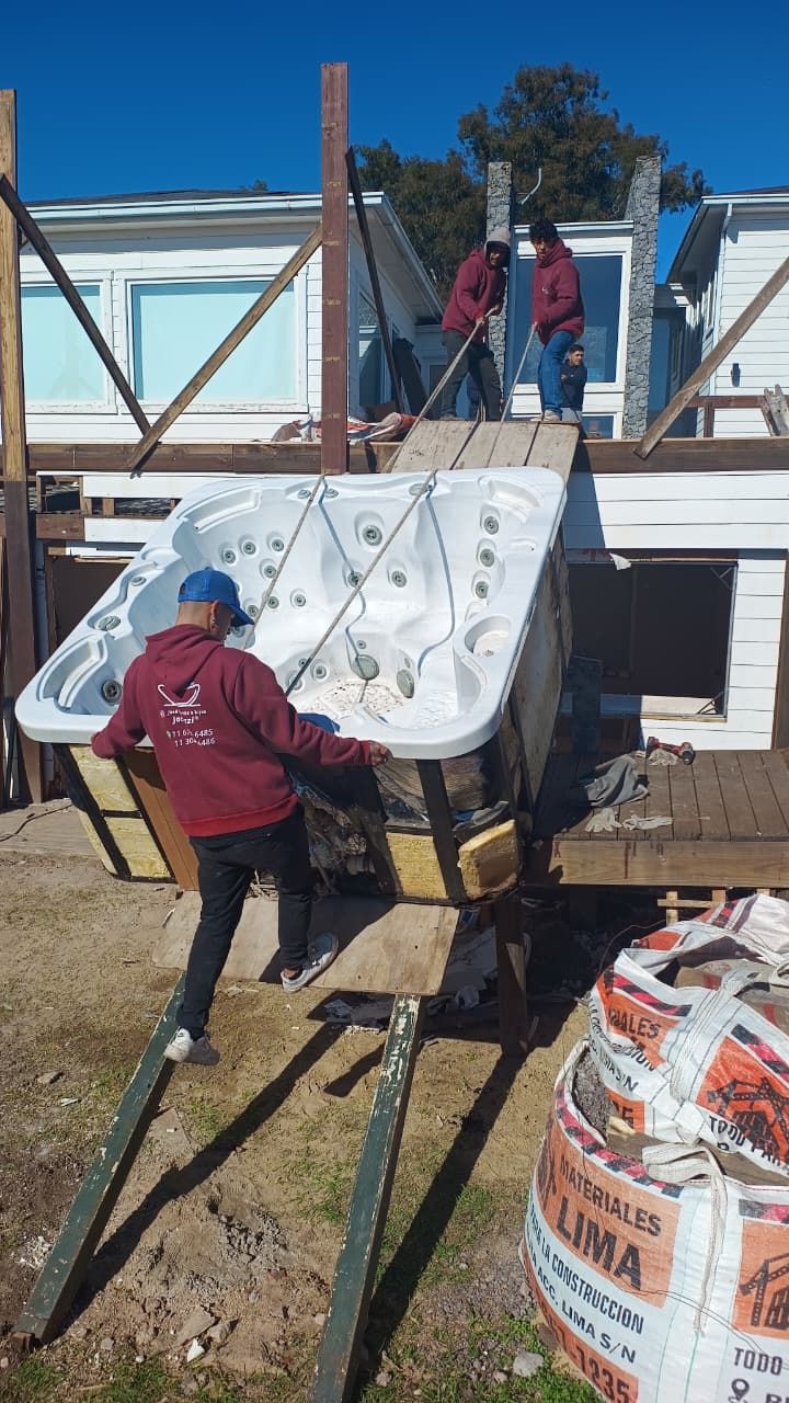 Hombres moviendo una bañera de hidromasaje por una rampa hacia una terraza; entorno de construcción.