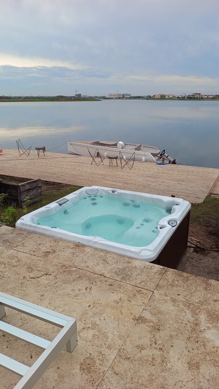 Jacuzzi en patio de hormigón con vistas a un lago tranquilo bajo un cielo nublado.