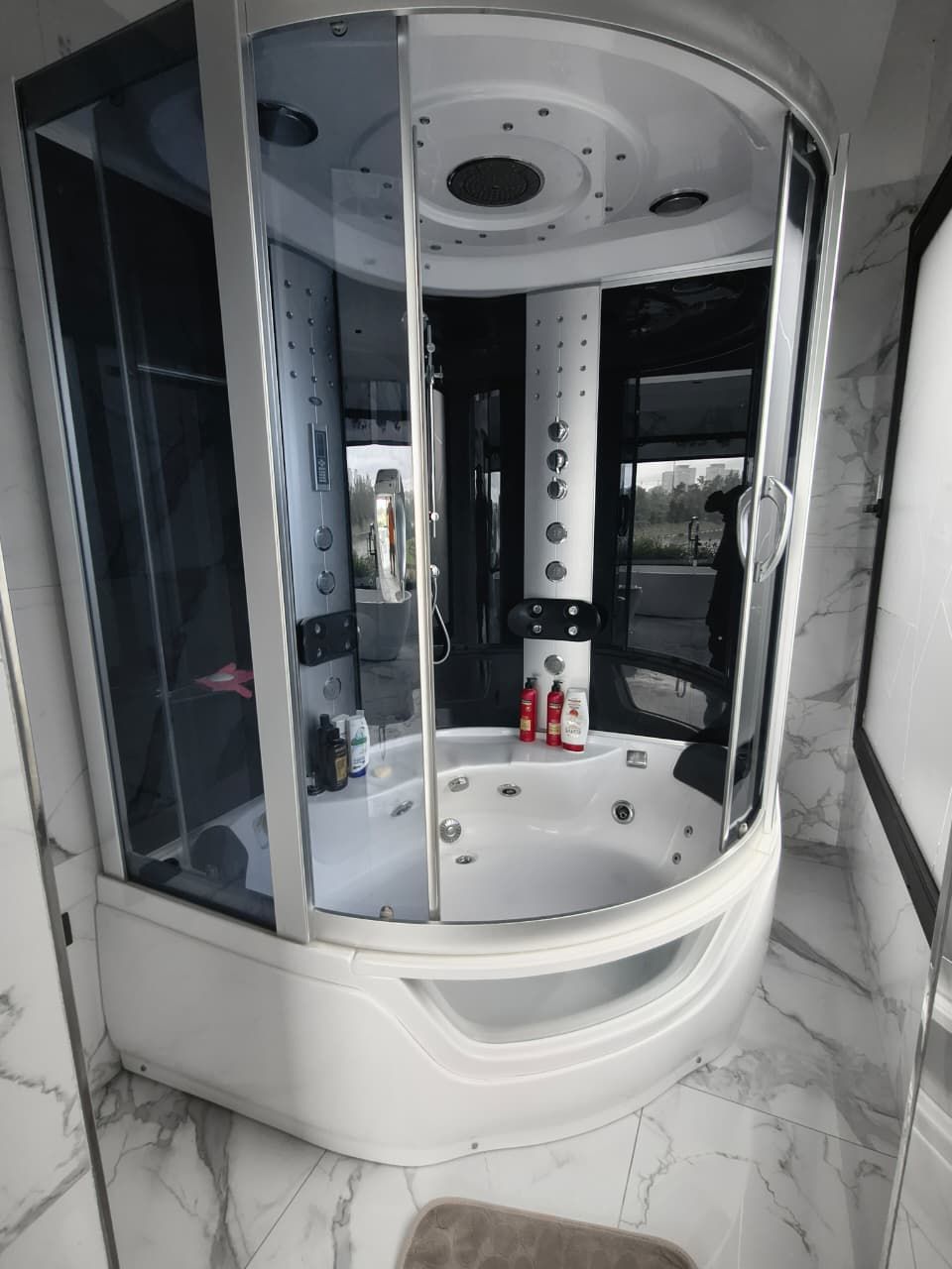 Ducha spa blanca y acristalada con chorros y bañera curva, en un baño.