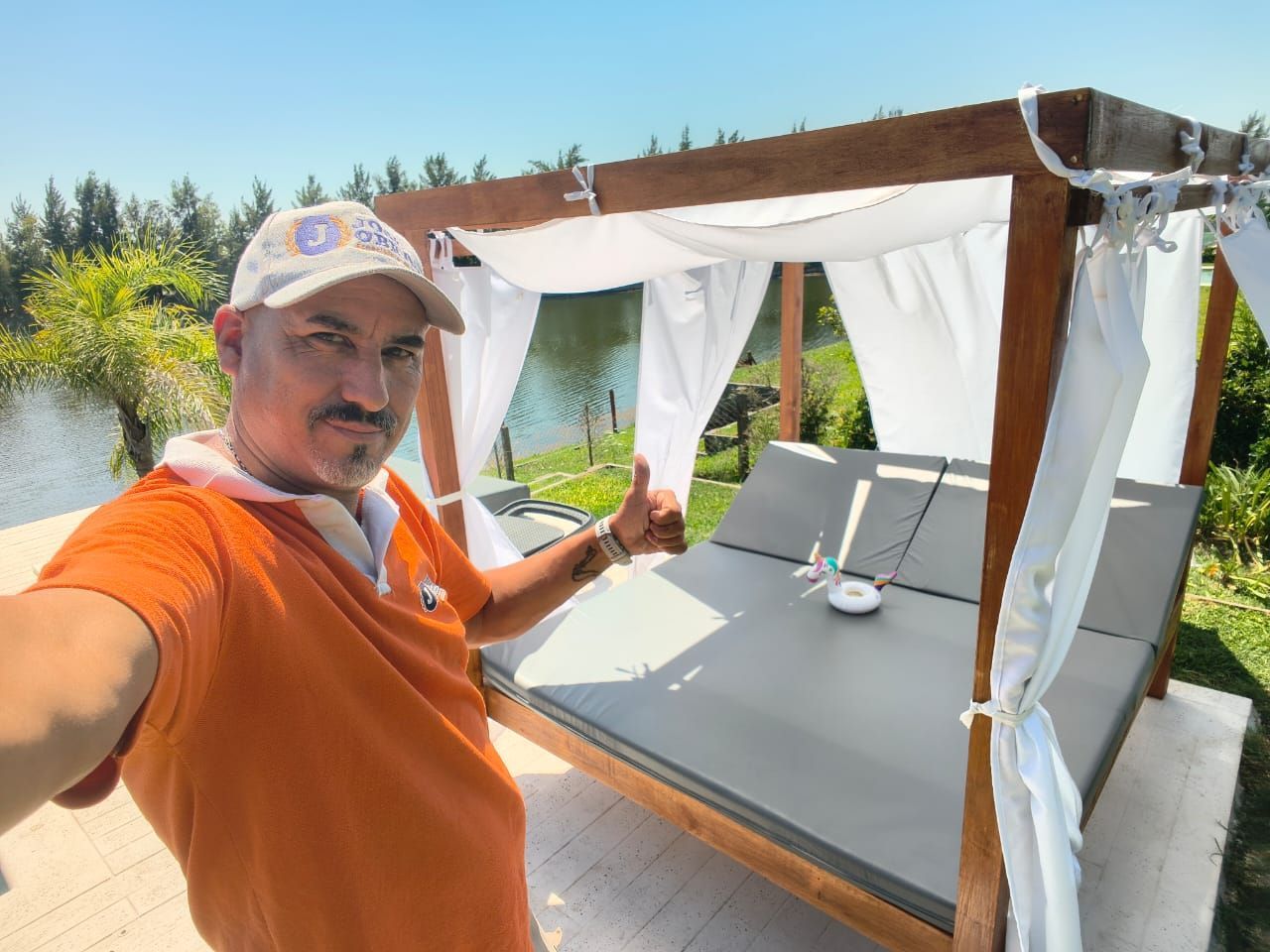 Un hombre con una camisa naranja hace un gesto de aprobación con el pulgar cerca de una cama.