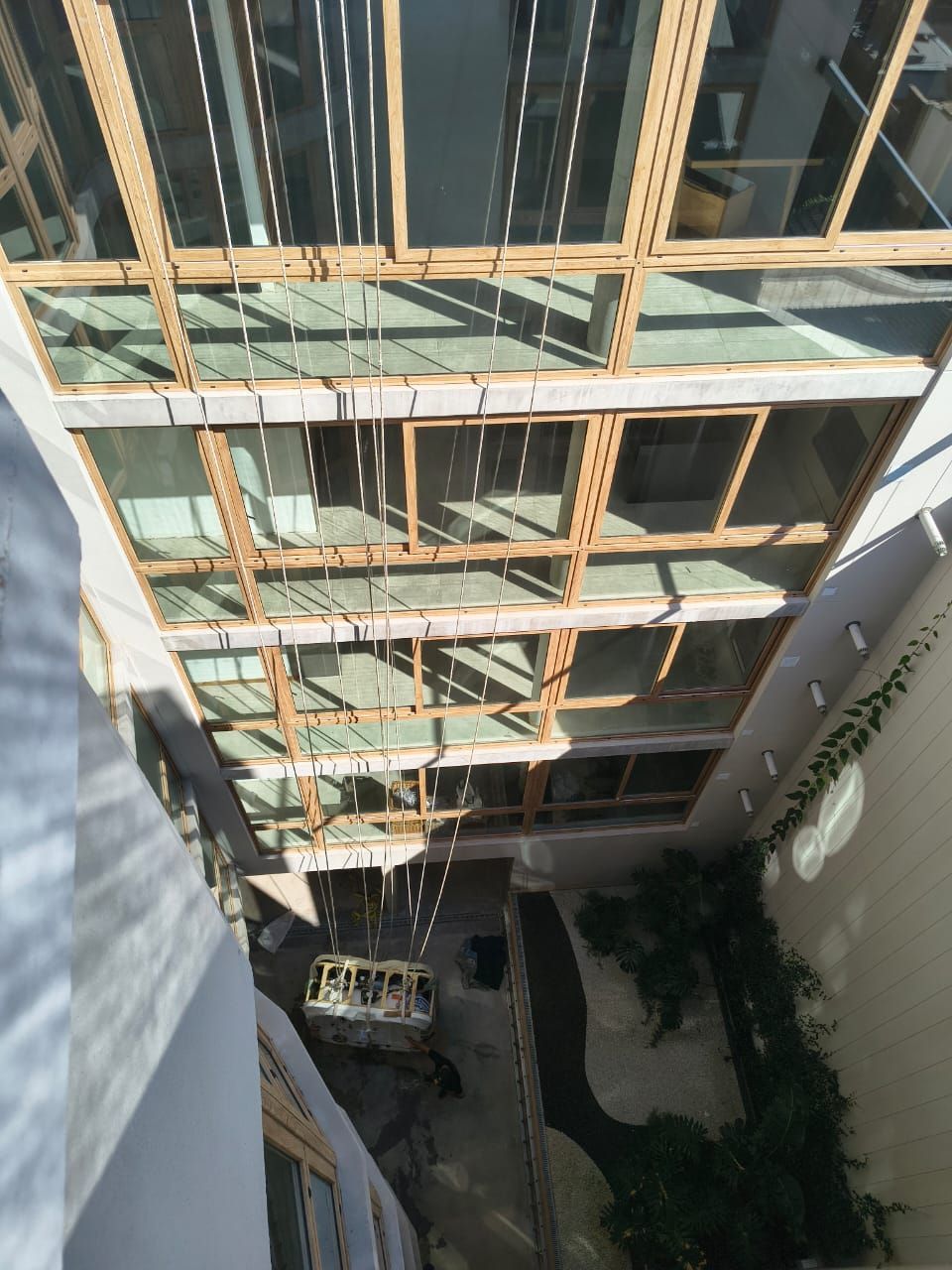 Mirando hacia abajo a un patio con techo de cristal, con un pequeño vehículo y vegetación debajo.