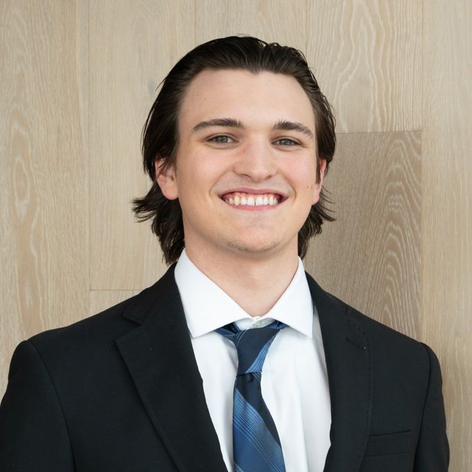 Smiling man in a black suit and blue tie against a wood-paneled background