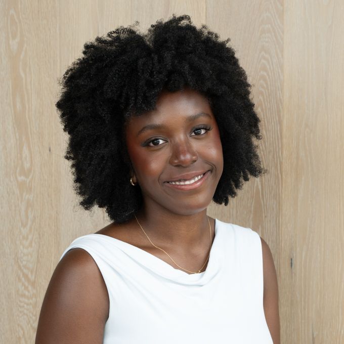 Smiling person in a white sleeveless top before a light wood wall