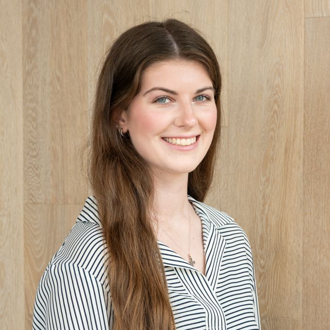 Smiling woman with long brown hair in a striped shirt against a wooden wall