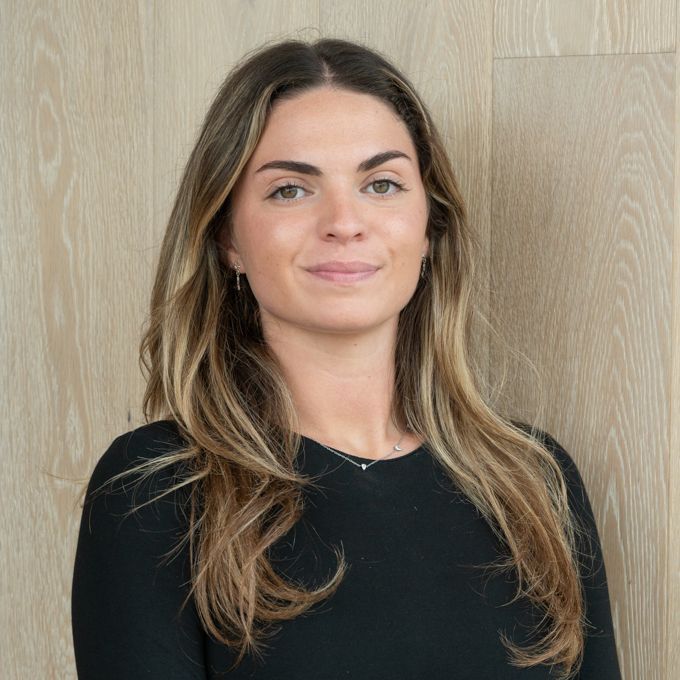 Portrait of a woman in a black top standing against a light wood wall