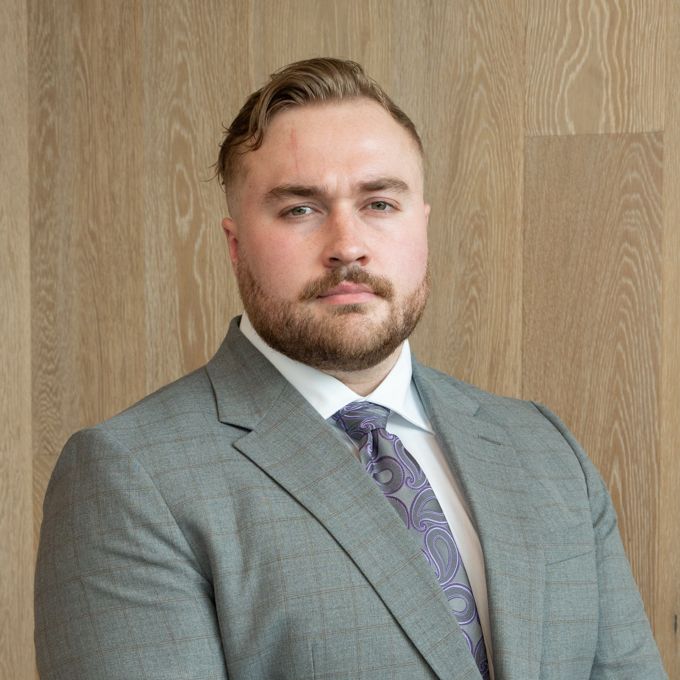 Man in a gray suit and purple tie posing against a wood-paneled wall