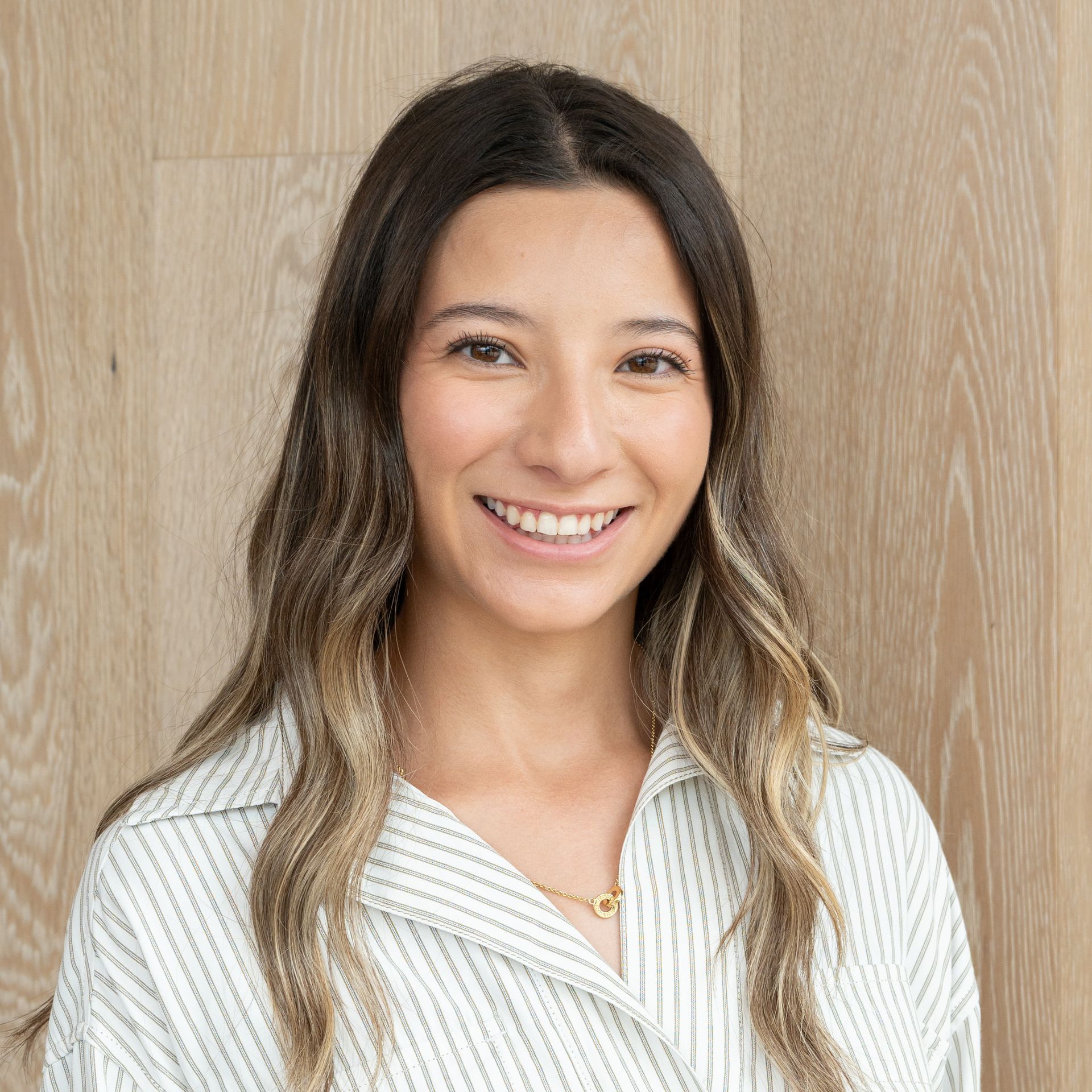 Smiling woman in a white striped blouse standing against a light wood wall