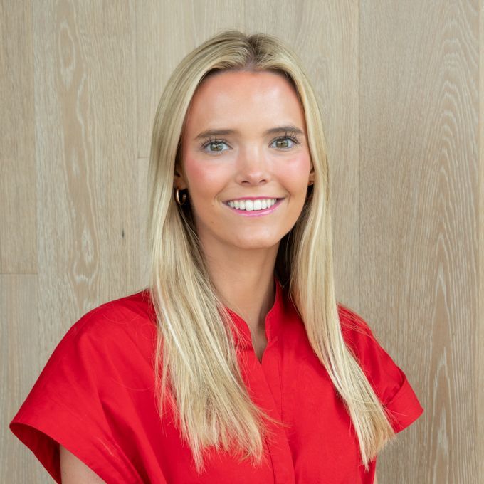 Smiling blonde woman in a red shirt against a light wood wall