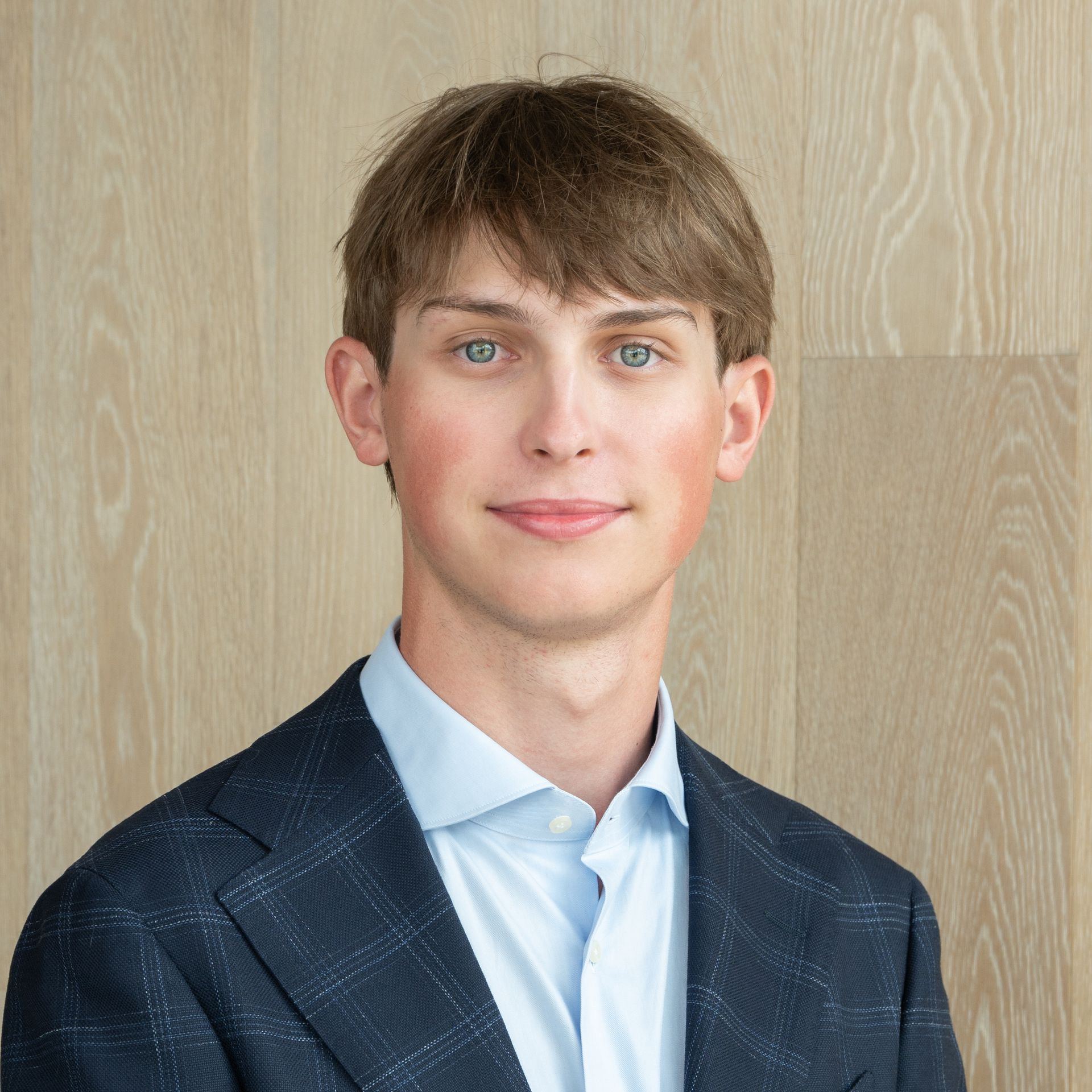 Portrait of a man in a dark blazer and light shirt against a wood-paneled background