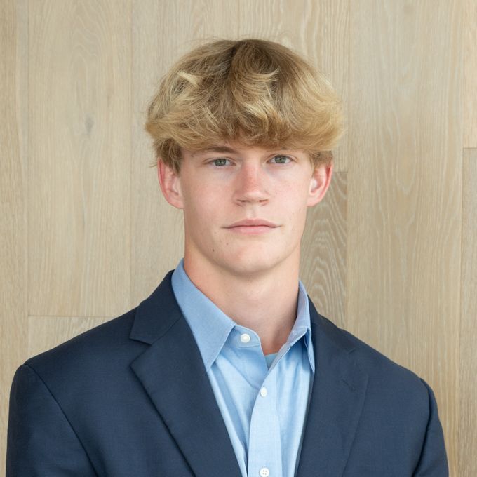 Young person in a navy blazer and light blue shirt against a light wood background