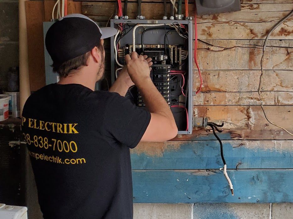 Un homme portant une chemise noire sur laquelle est écrit « electrick » travaille sur un boîtier électrique
