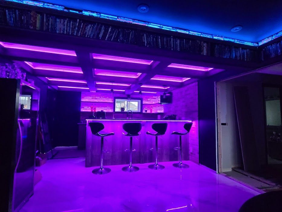 Un bar avec des lumières violettes au plafond et des tabourets.