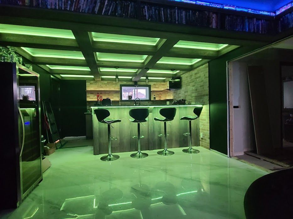 Une cuisine avec un bar et des tabourets et des lumières vertes au plafond.