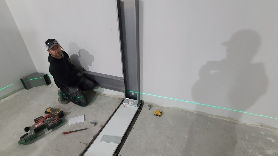 Un homme est agenouillé dans une pièce en utilisant un niveau laser.