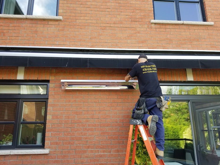 Un homme se tient debout sur une échelle en train de fixer un auvent sur le côté d'un bâtiment en briques.