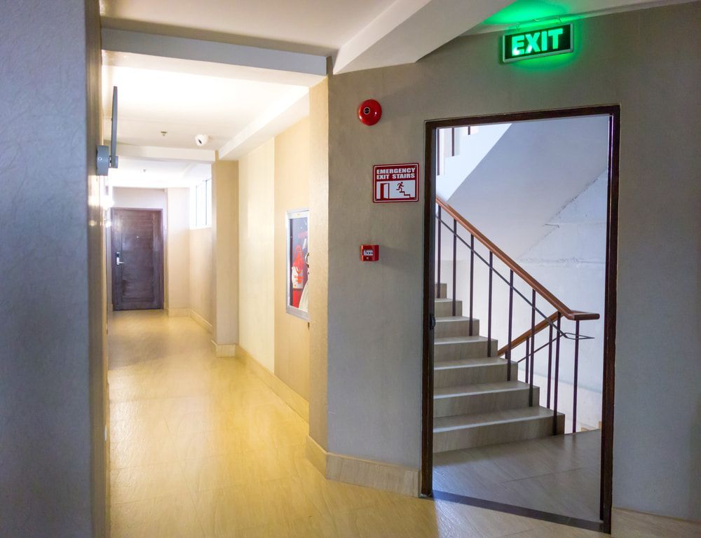 A Hallway with Stairs and An Exit Sign on The Wall — Test Right Services in Kirwan, QLD
