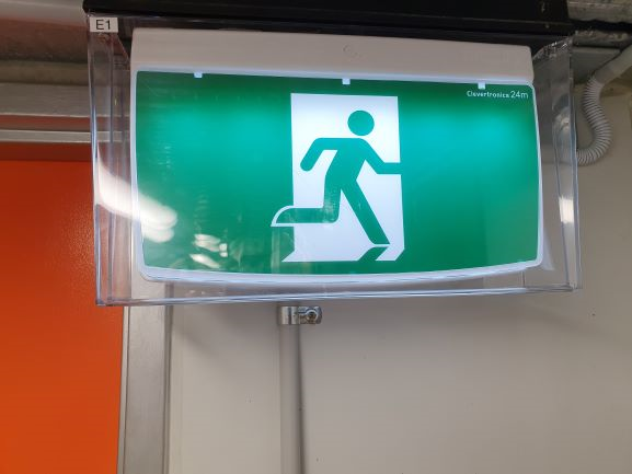 An Emergency Exit Sign Is Hanging from The Ceiling of A Hallway — Test Right Services in Charters Towers, QLD
