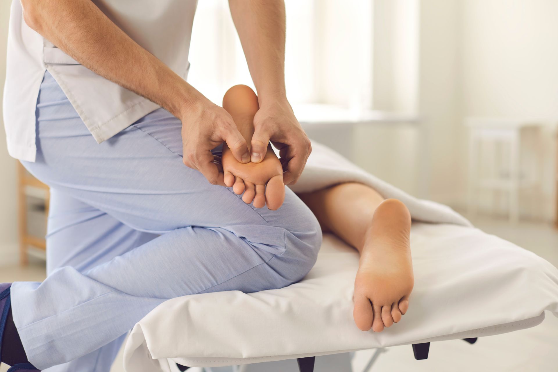 A professional practitioner performs a foot massage on a person lying on a massage table in a bright, clinical space.