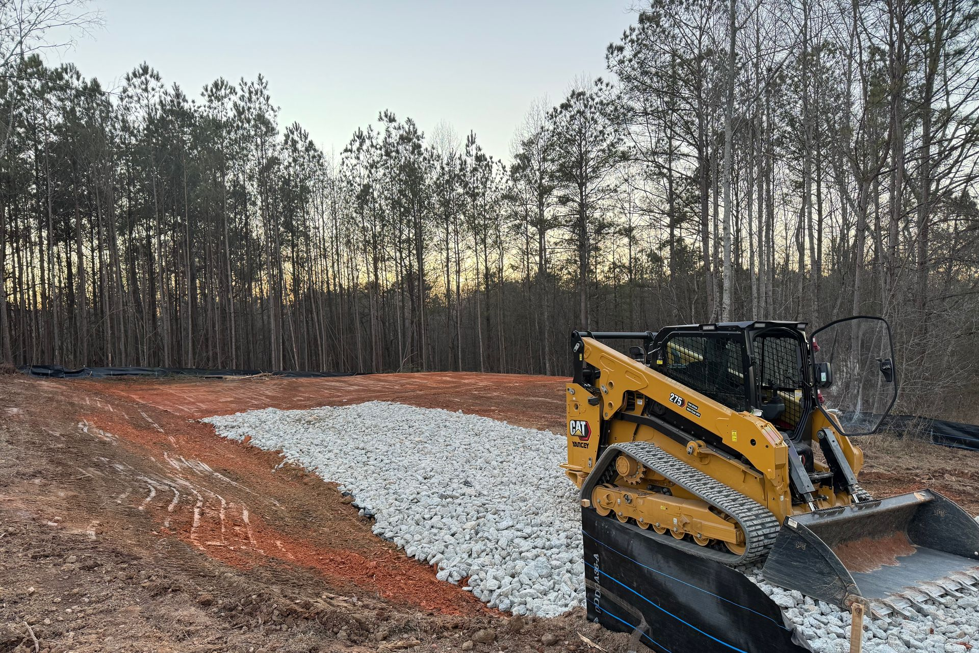 Two yellow excavators stir up clouds of dust while moving red earth at a construction site backed by a line of trees. Two yellow excavators stir up clouds of dust while moving red earth at a construction site backed by a line of trees.