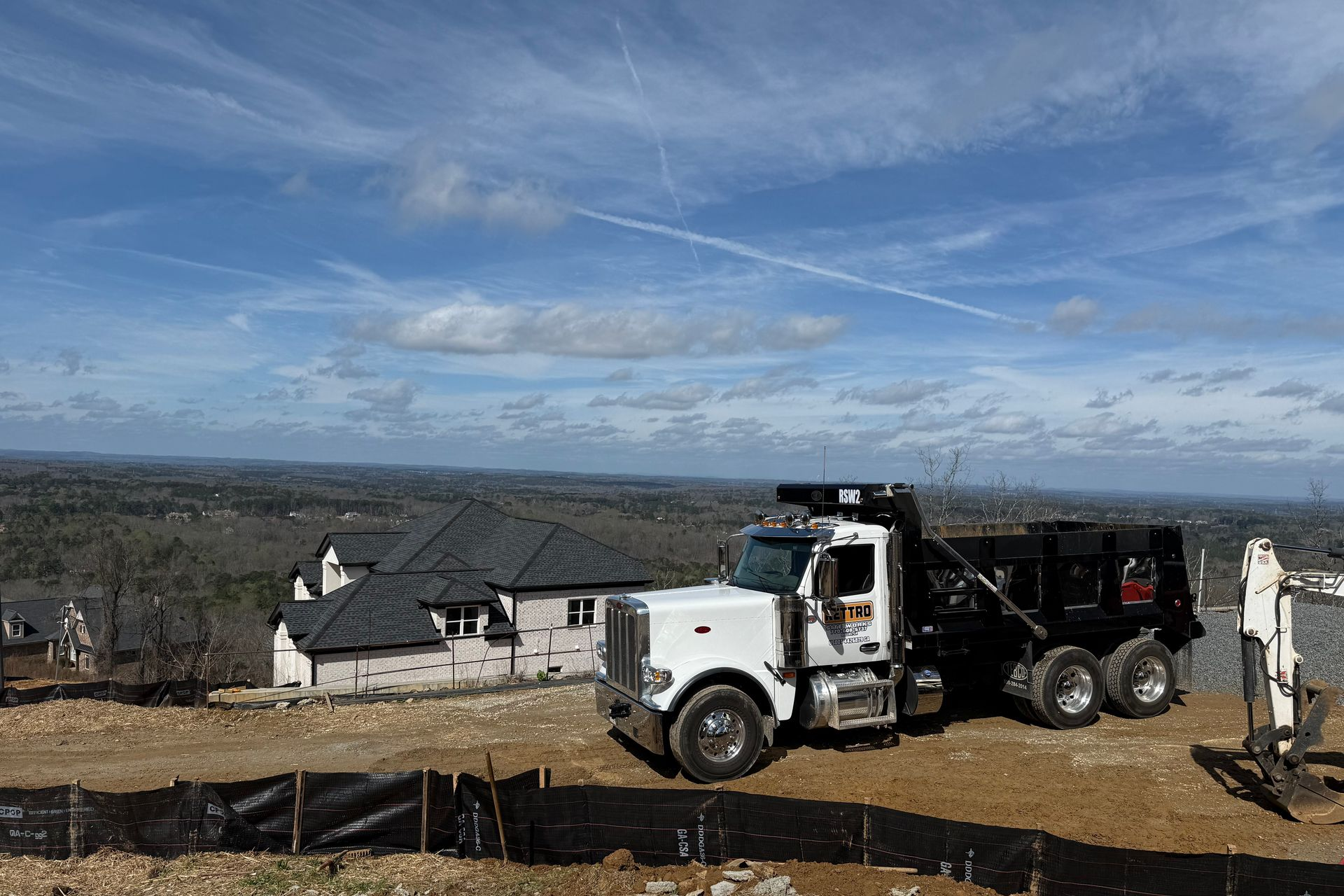 A semi-truck with a flatbed trailer carrying a yellow construction loader, parked on a roadside under a clear blue sky. A semi-truck with a flatbed trailer carrying a yellow construction loader, parked on a roadside under a clear blue sky.