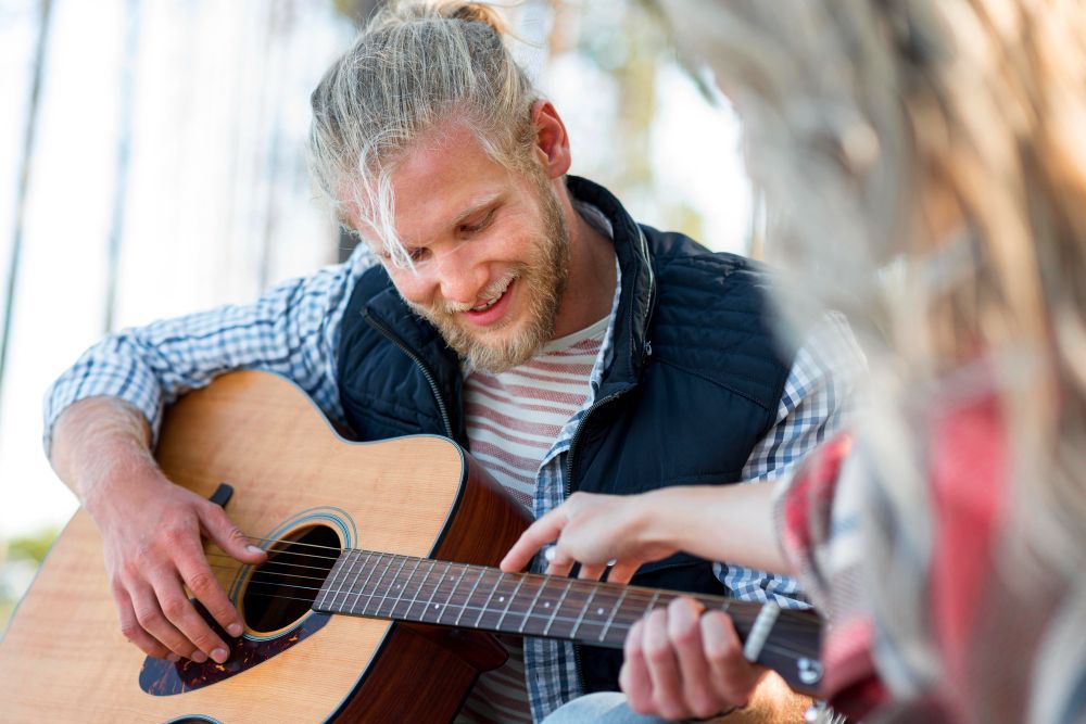 Een man speelt akoestische gitaar terwijl een vrouw buiten naar de toetsen wijst.