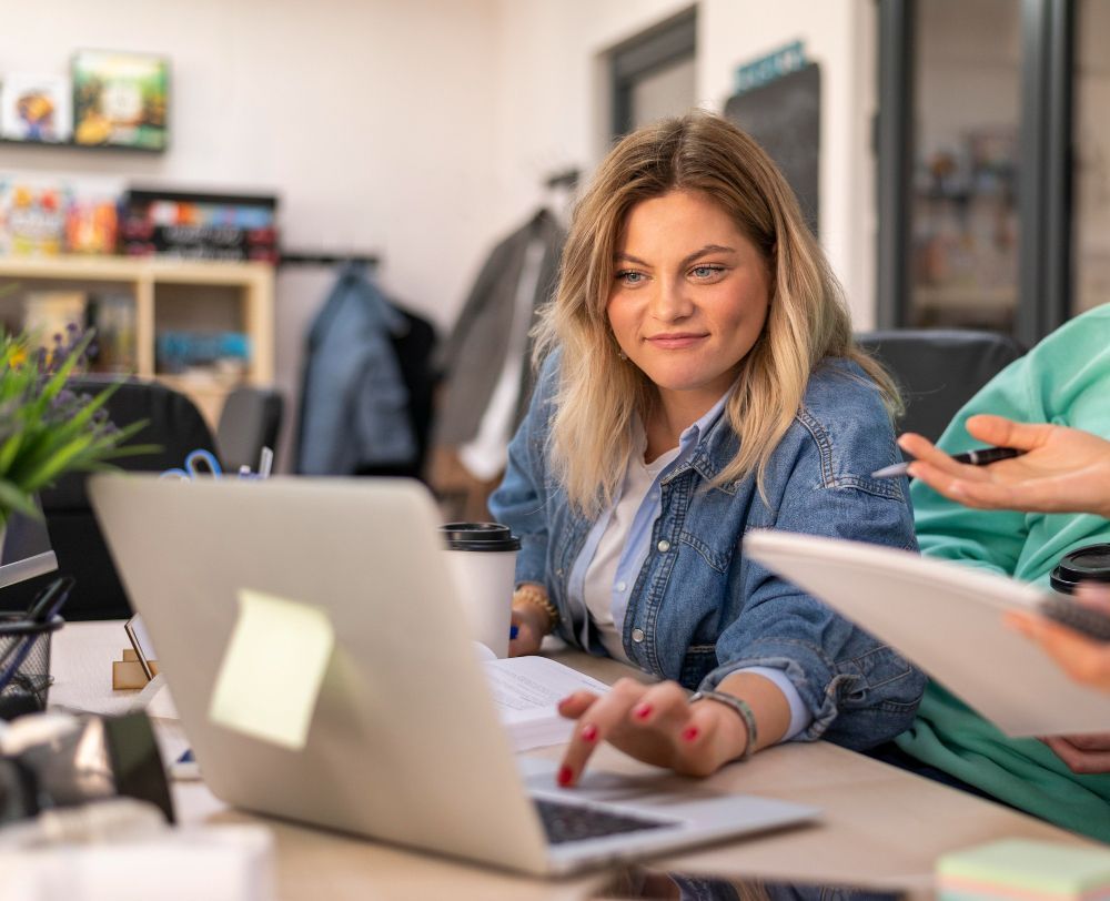 Vrouw zit aan een bureau en gebruikt een laptop, terwijl ze geconcentreerd naar het scherm kijkt.
