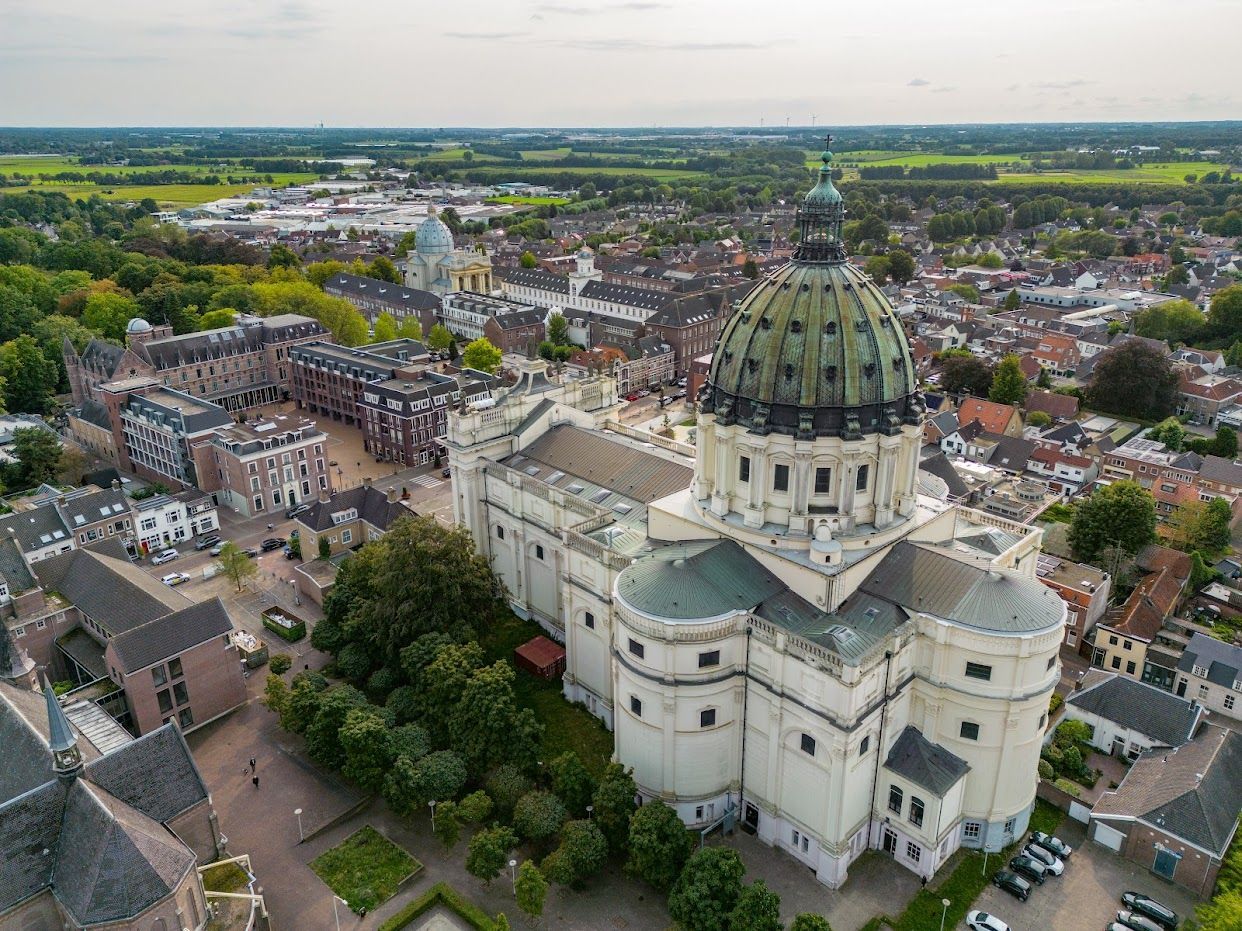 Luchtfoto van een grote witte kerk met een groene koepel in een stedelijke omgeving.