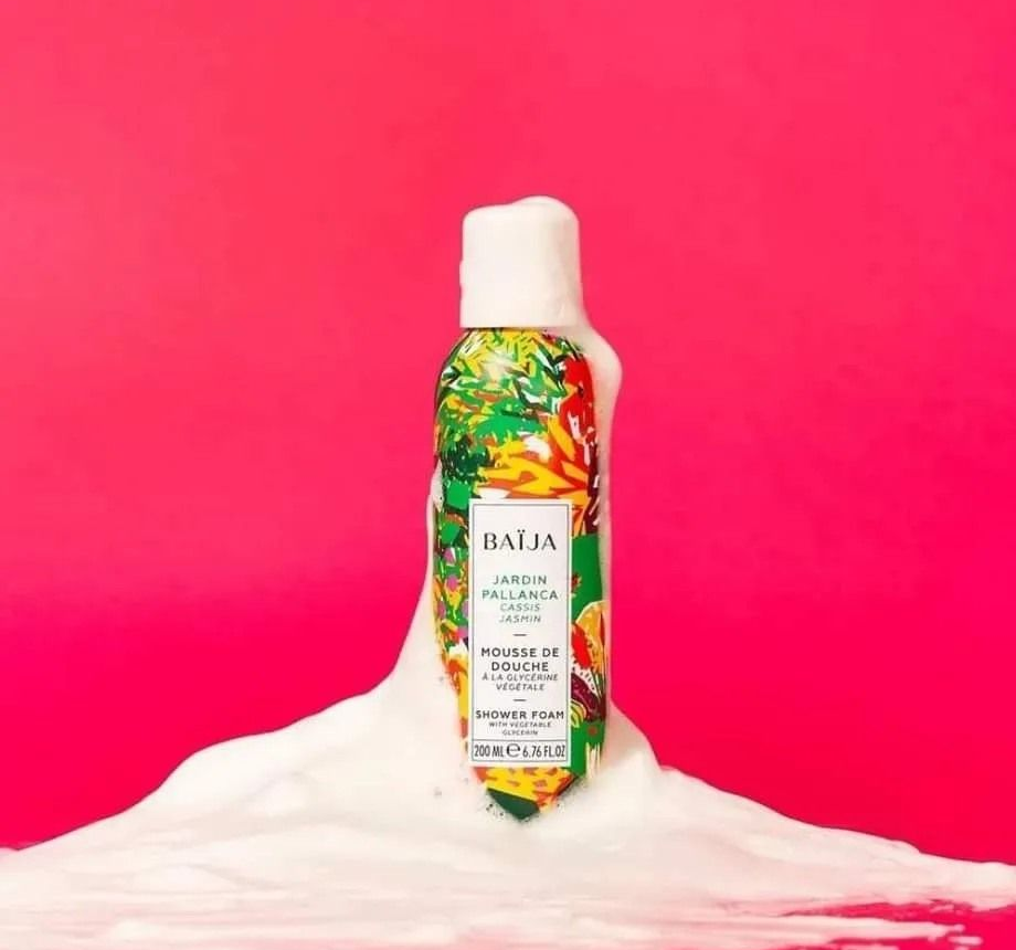 Flacone di schiuma per il corpo Ballaia con etichetta colorata, su uno strato di schiuma bianca su sfondo rosa.