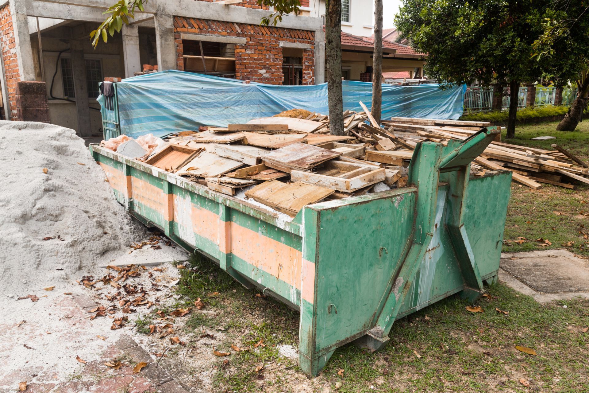 Green dumpster overflowing with construction debris, next to a building under construction.